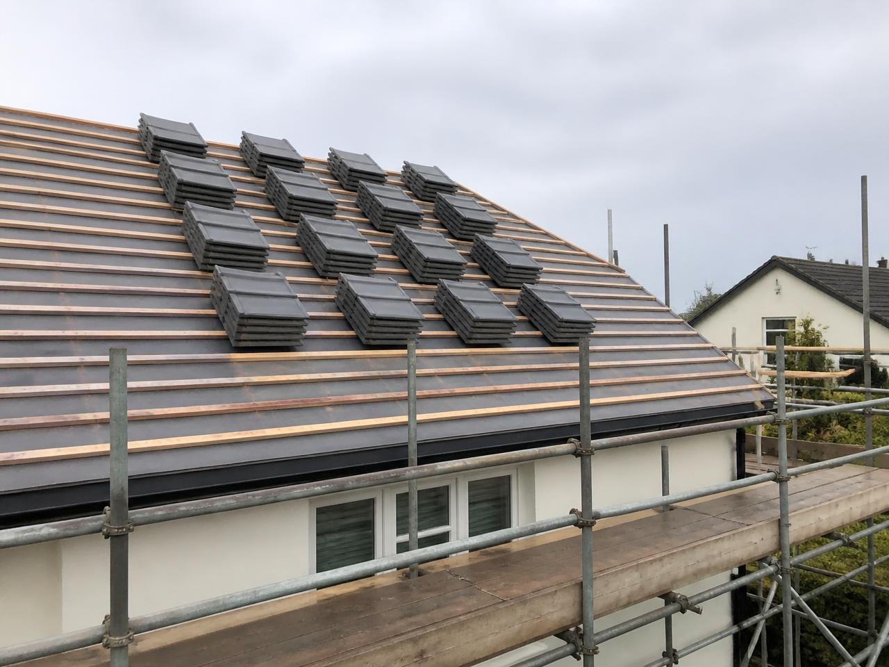 A pitched roof stripped back to breathable membrane and new timber battens, with stacks of new grey tiles ready to lay