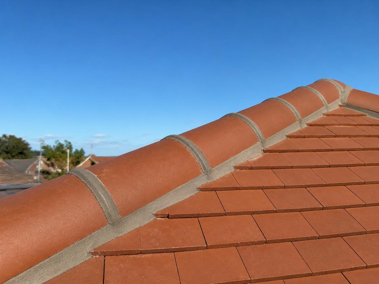 A run of clay ridge tiles freshly bedded and pointed along a roof apex against blue sky