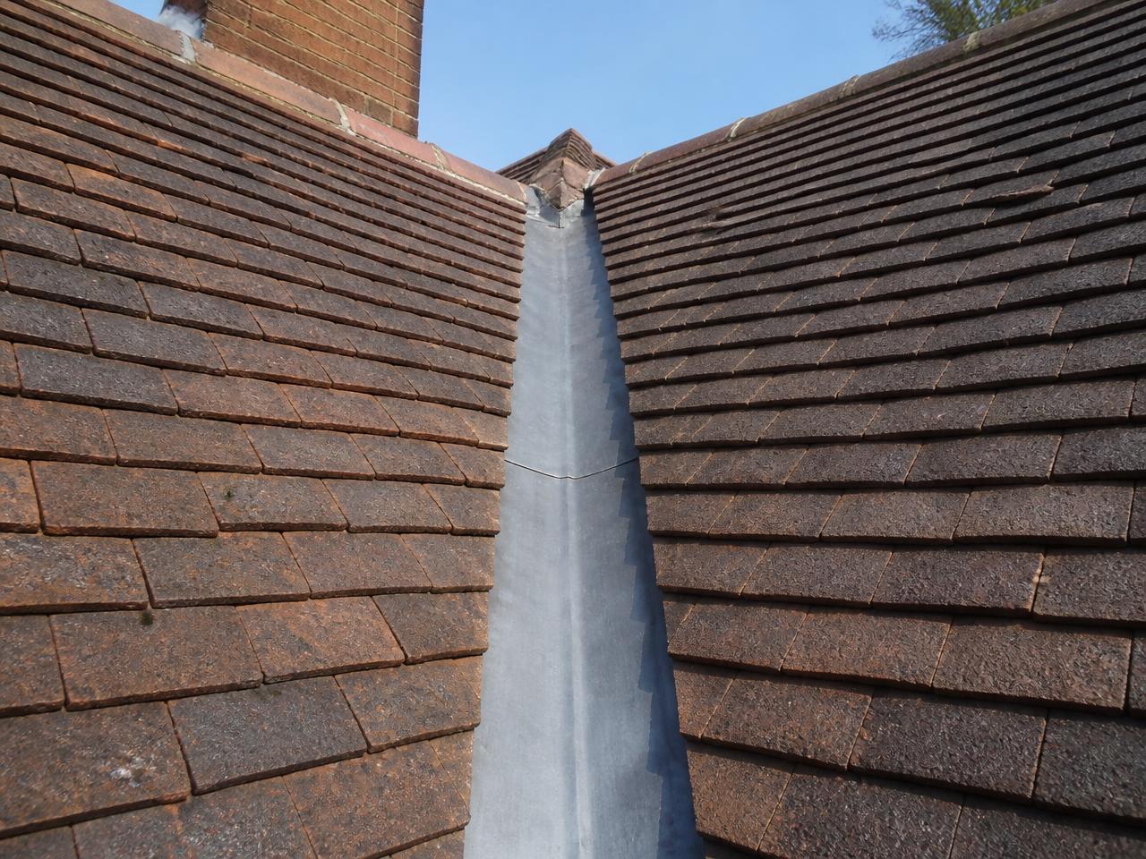 A lead valley running between two tiled roof slopes with tiles cut cleanly to the line